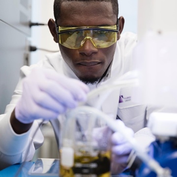 Male student wearing lab coat and goggles working on a project