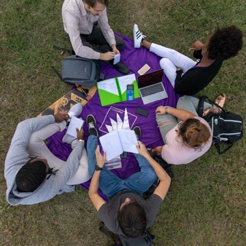 Students sitting outside with open laptops and notebooks